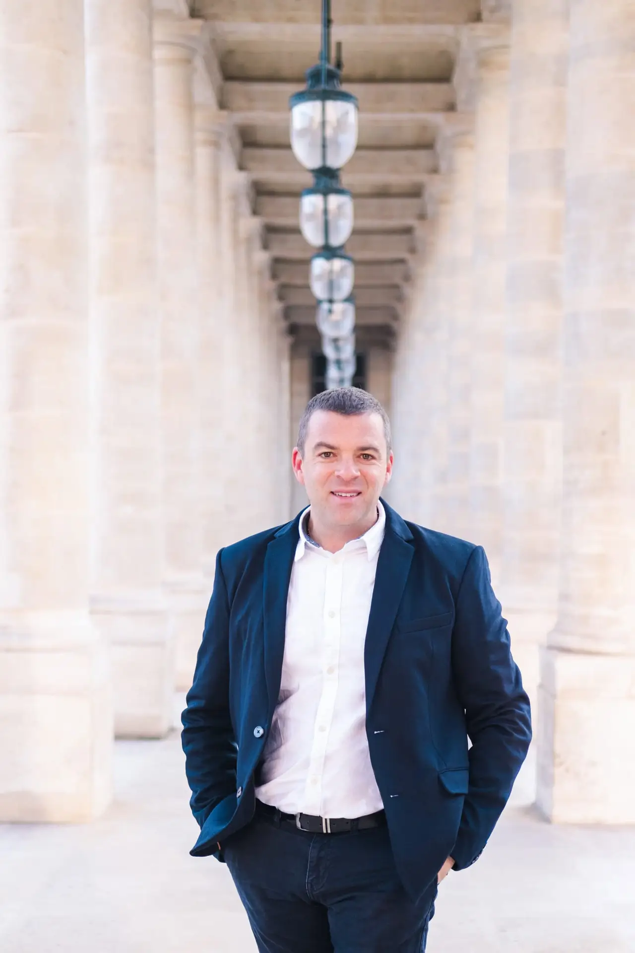 Portrait du photographe Julien Boyer sous une galerie de colonnes à Paris, lumière douce et ambiance élégante.