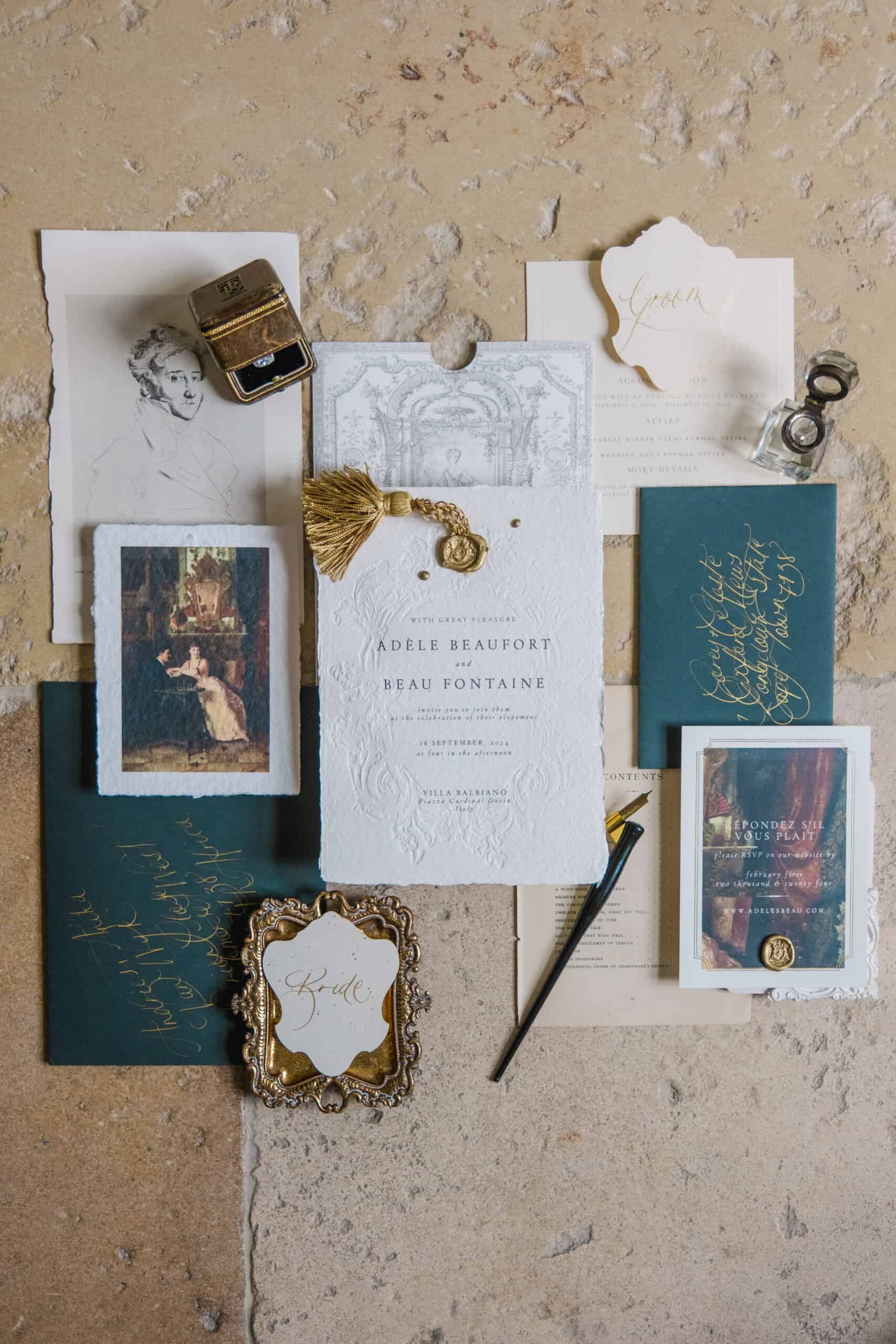 Flatlay de papeterie de mariage luxueuse au style ancien, avec calligraphie dorée et bague vintage, sur pierre naturelle.