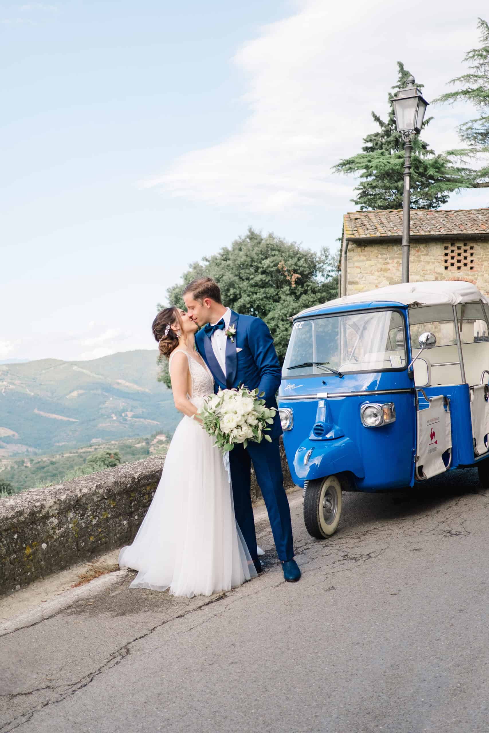 Bride and groom kissing beside blue vintage Piaggio Ape, Tuscan countryside wedding
