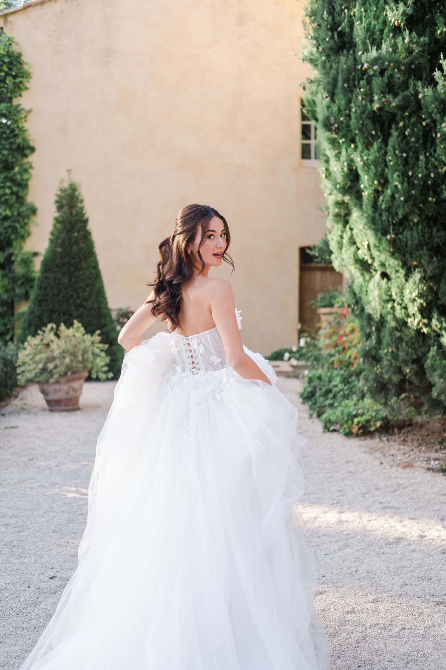 Elegant bride in flowing gown walking through a Provence estate garden during golden hour – destination wedding photography in the South of France.