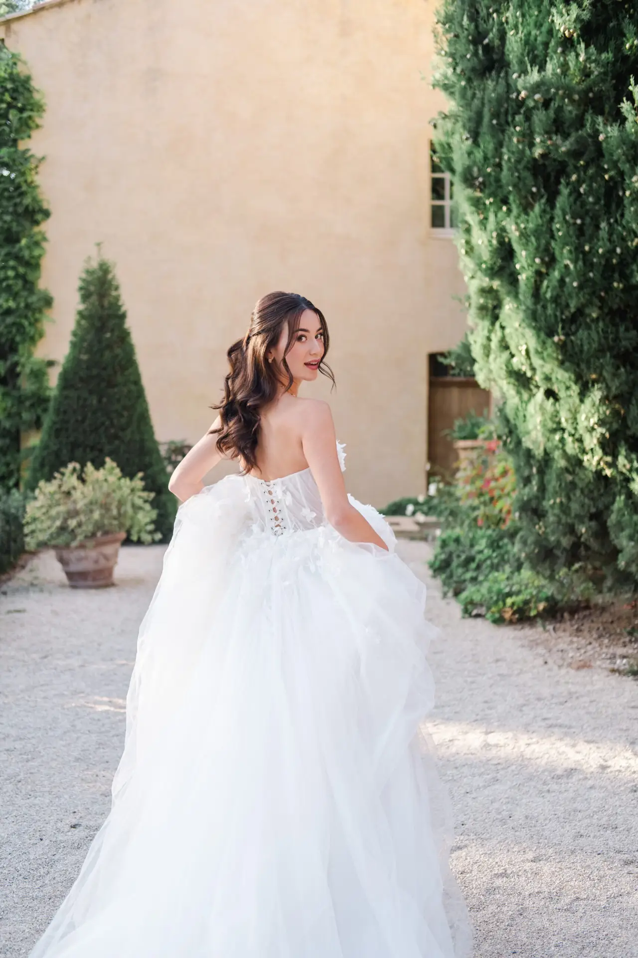 Elegant bride in flowing gown walking through a Provence estate garden during golden hour – destination wedding photography in the South of France.
