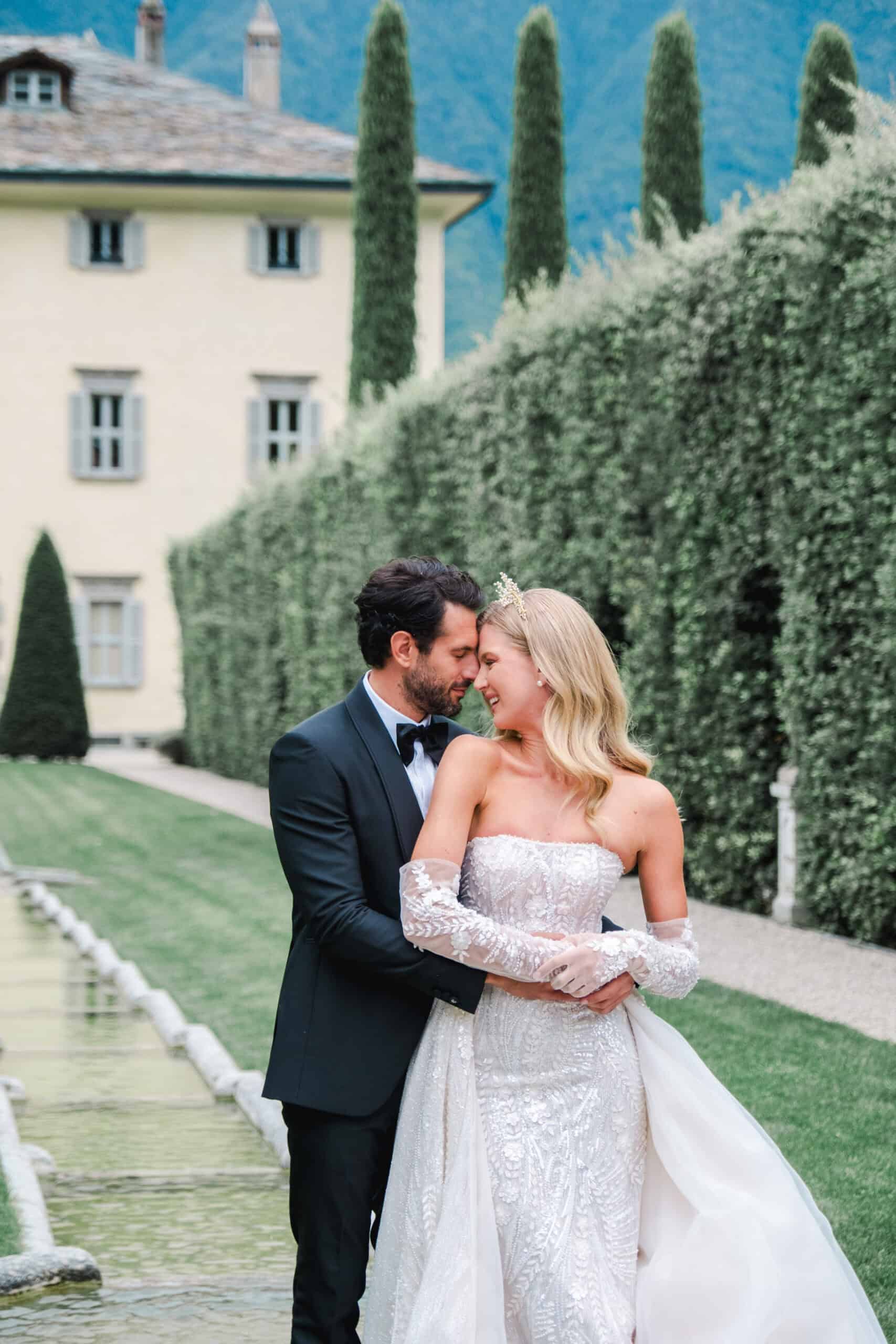 Moment tendre entre les mariés enlacés dans les jardins de la Villa Balbiano, devant les haies parfaitement taillées.