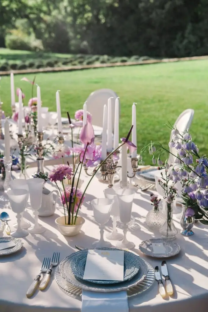 Wedding reception table outdoors with white candles and purple floral arrangements