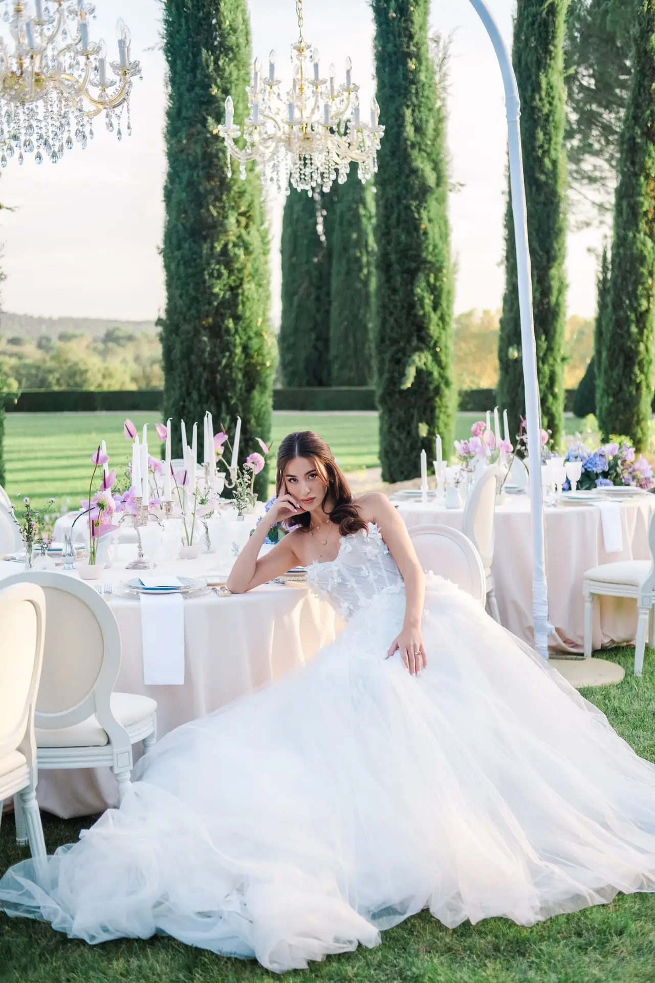 Bride in a white gown seated elegantly by a decorated wedding table at Château de la Gaude