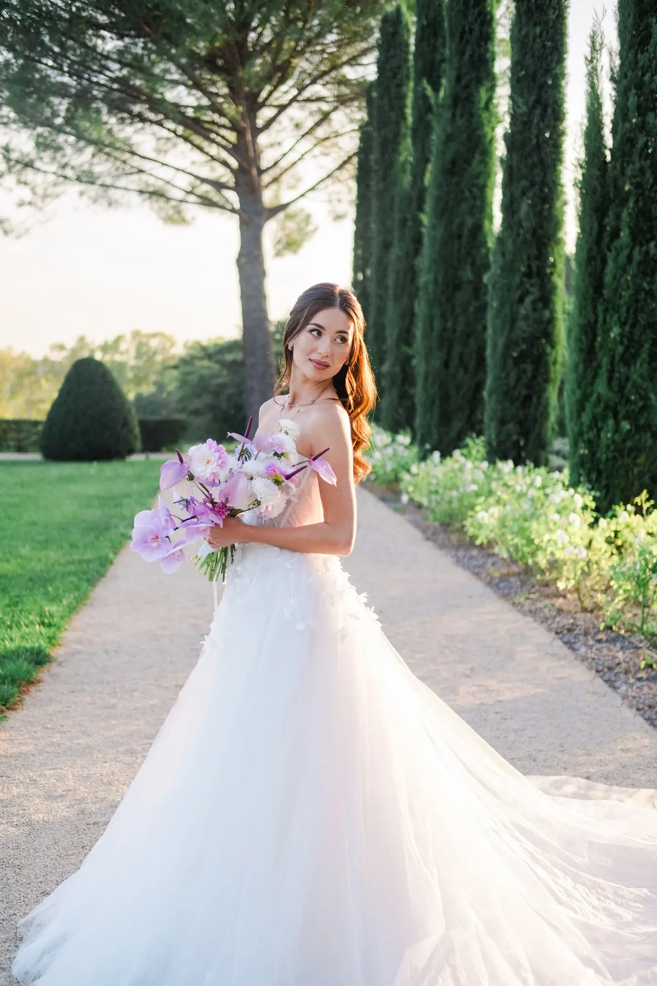 Bride holding a purple bouquet, standing in the gardens of Château de la Gaude