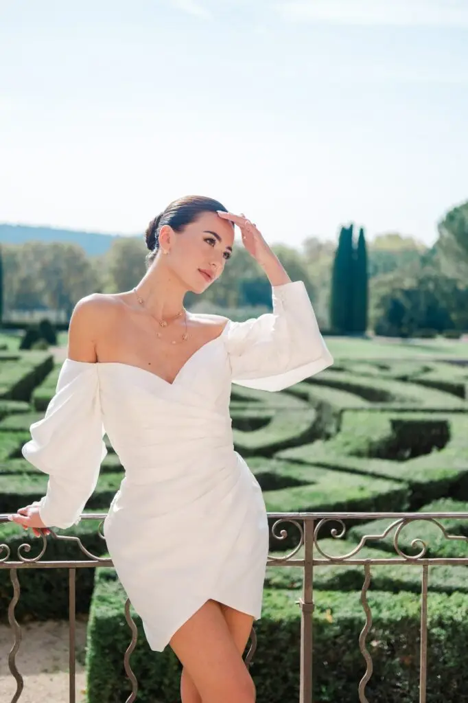 Bride in short white dress posing by a balcony railing overlooking the gardens of Château de la Gaude