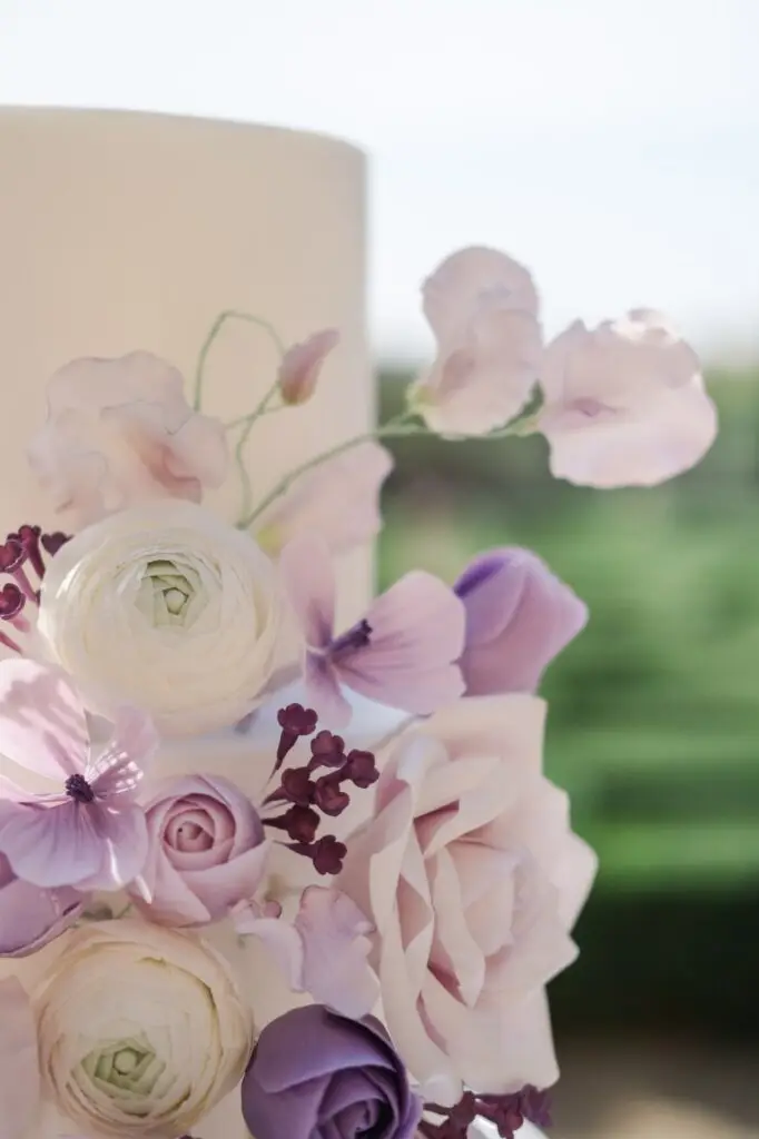Close-up of wedding cake decorated with pastel sugar flowers in pink, white, and purple