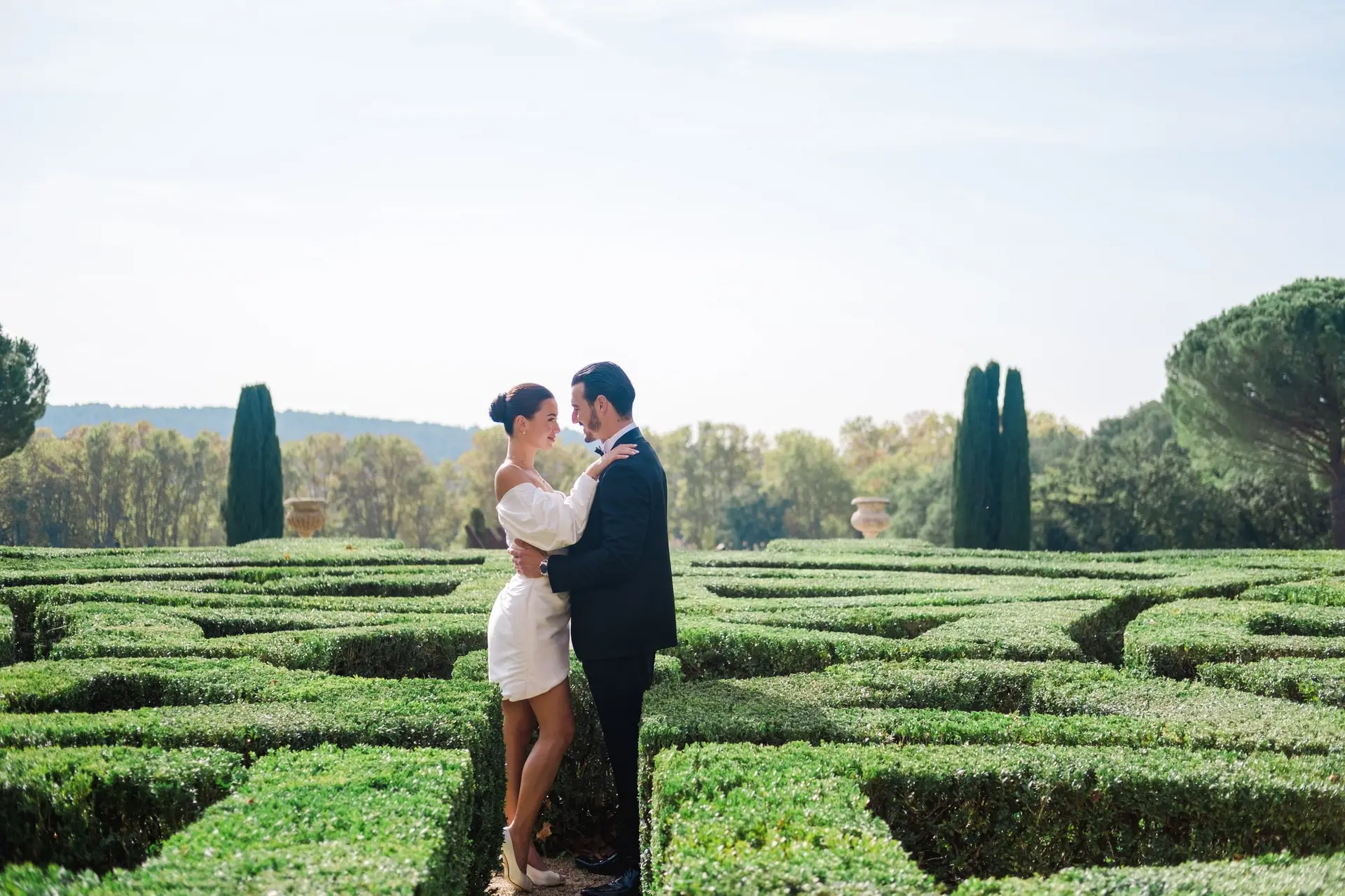 Romantic moment as the bride and groom embrace in the sunlit labyrinth gardens of Château de la Gaude