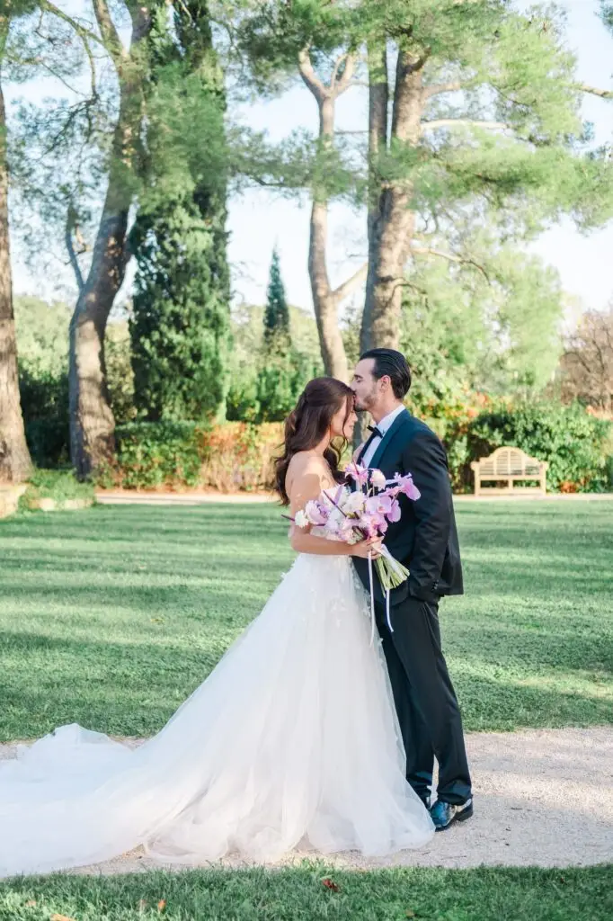 Bride and groom embracing in the gardens of Château de la Gaude, bride holding a purple bouquet.