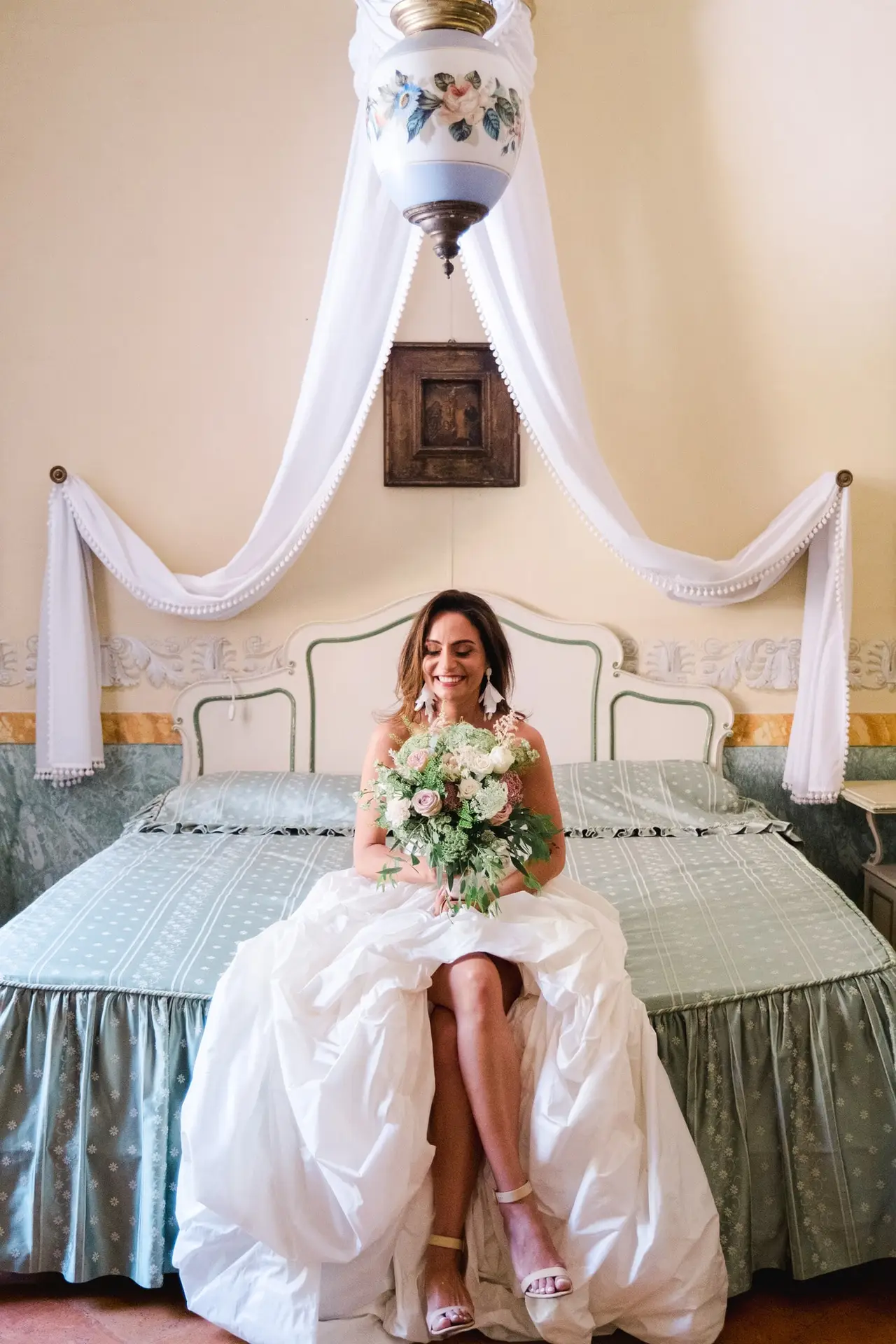 Seated gracefully in her bridal suite, bouquet in hand, the bride exudes timeless elegance. Her gown flows around her, blending romance and sophistication inside this historic Italian villa.