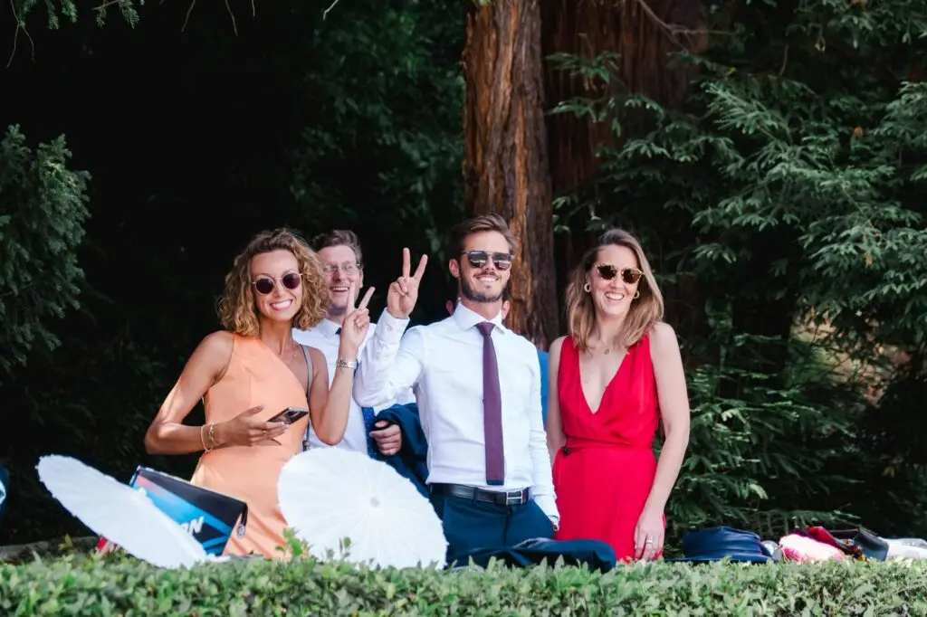 A joyful group of guests in colorful attire, smiling and flashing peace signs while enjoying the outdoor celebration.