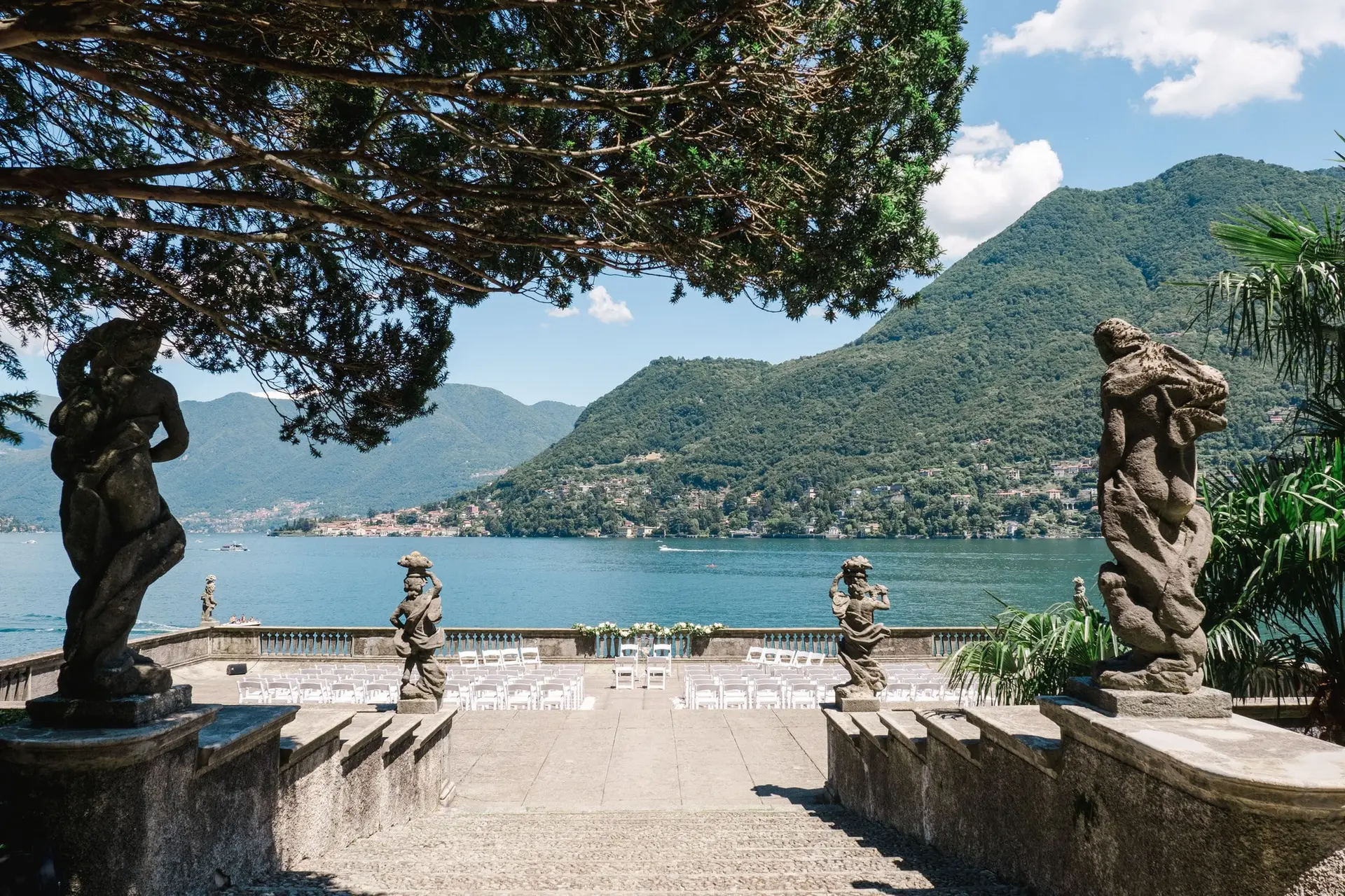 A breathtaking view of the ceremony setup overlooking Lake Como, framed by grand statues and lush mountains.