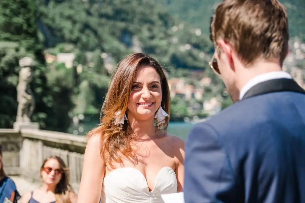 Bride smiling with emotion during the ceremony, the Italian lake and mountains in the background.