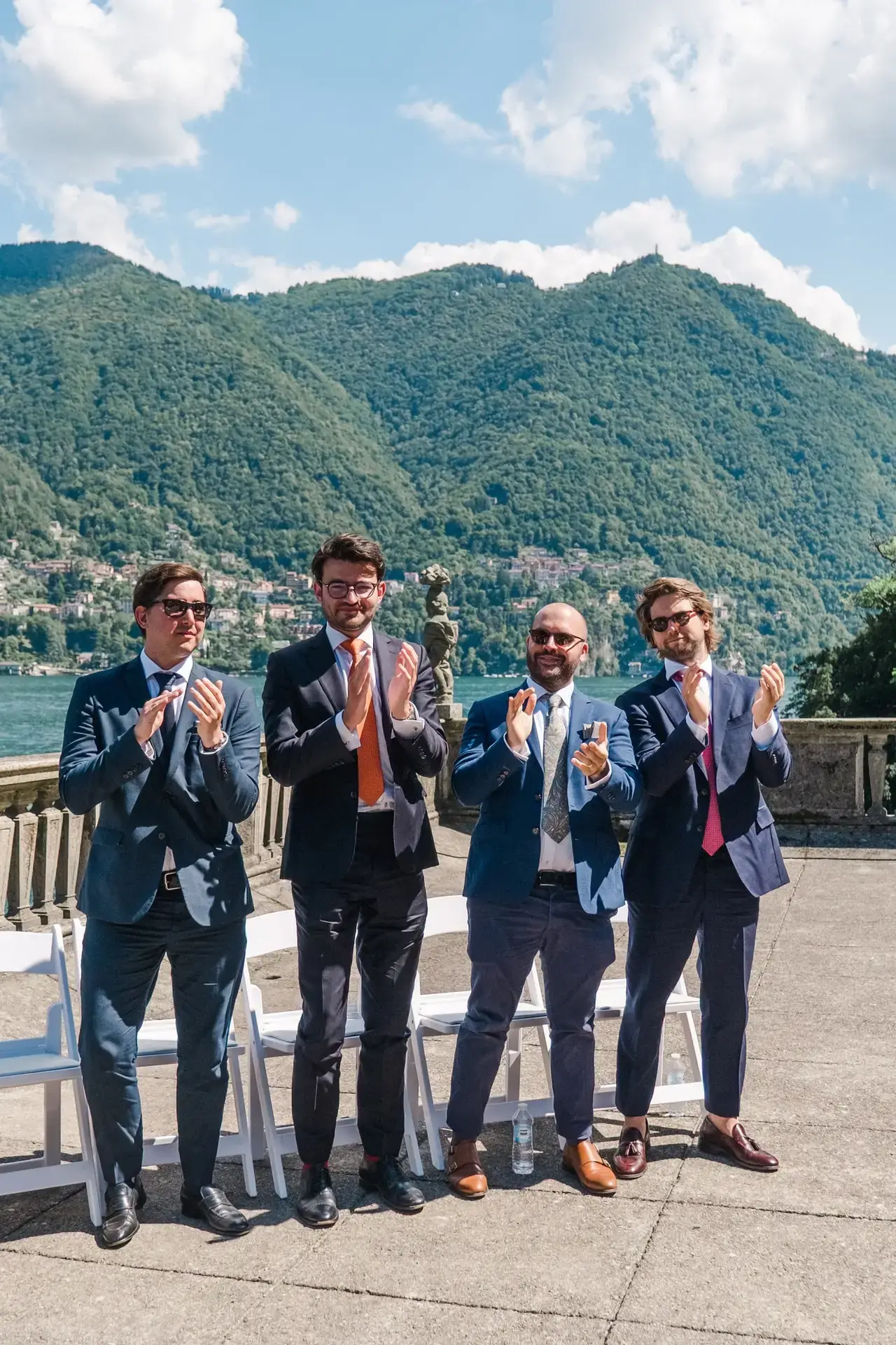 Groomsmen standing and applauding the couple against the dramatic mountain views of Lake Como.