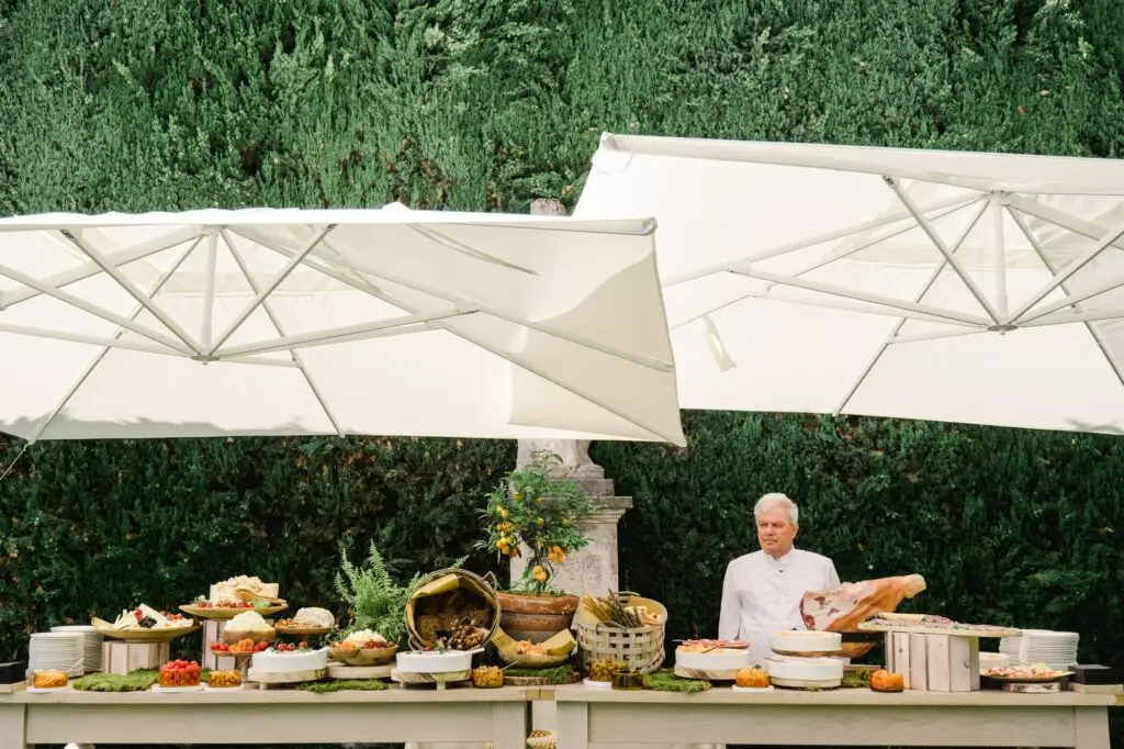 Outdoor Italian buffet with chef and traditional antipasti served under white umbrellas during a Lake Como wedding.