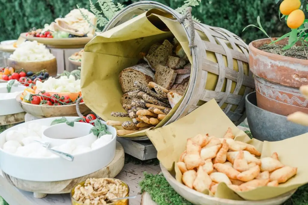 Rustic bread basket with Italian focaccia, breadsticks, and fresh vegetables on a wedding buffet table.