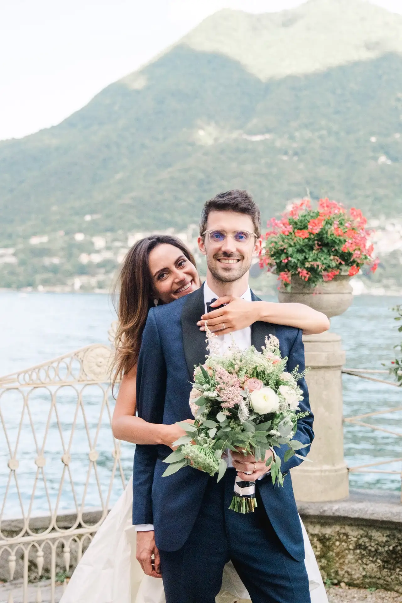 Bride embracing the groom from behind with Lake Como in the background, captured by Julien Boyer, French wedding photographer.