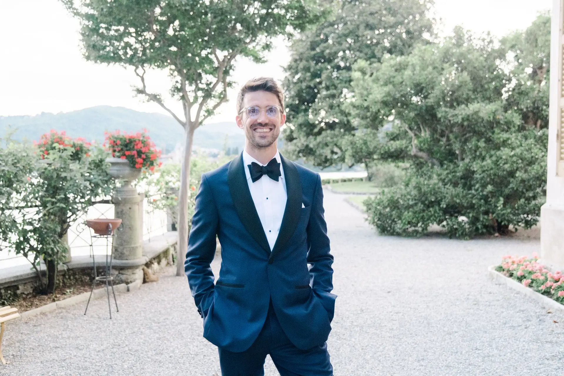 Groom standing in a navy tuxedo with bow tie, smiling confidently at Villa Pizzo, Lake Como.