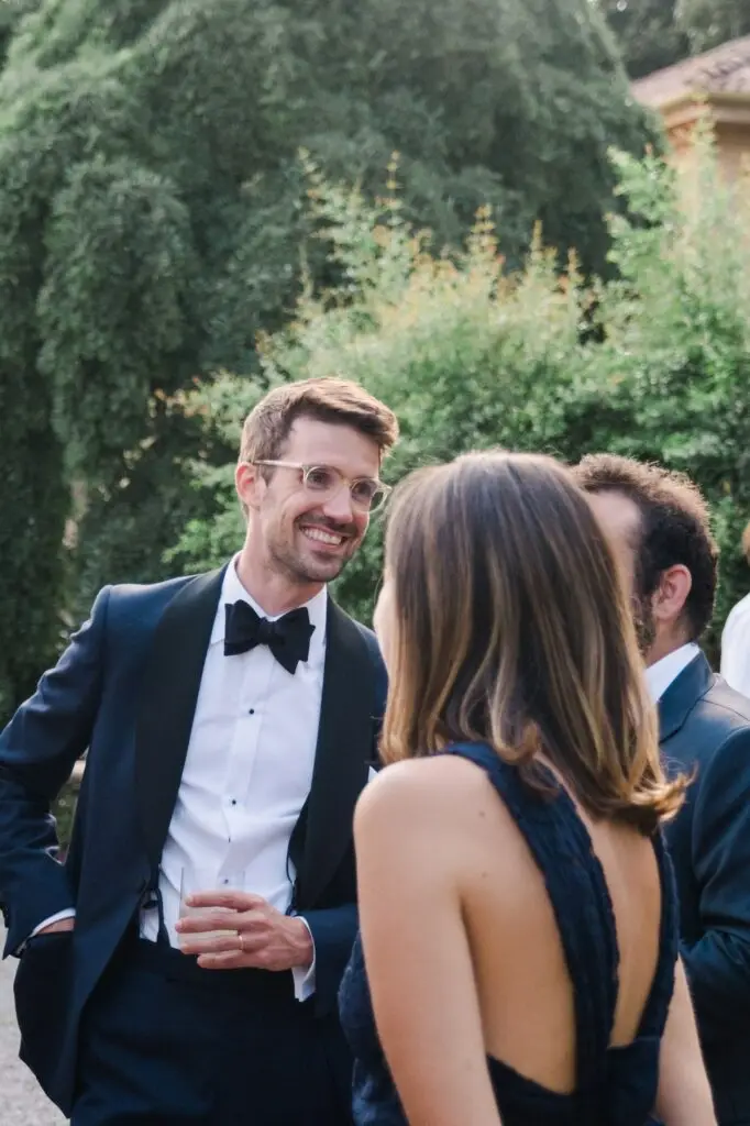 Groom enjoying a conversation with guests during cocktail hour at Villa Pizzo, holding a drink in hand.