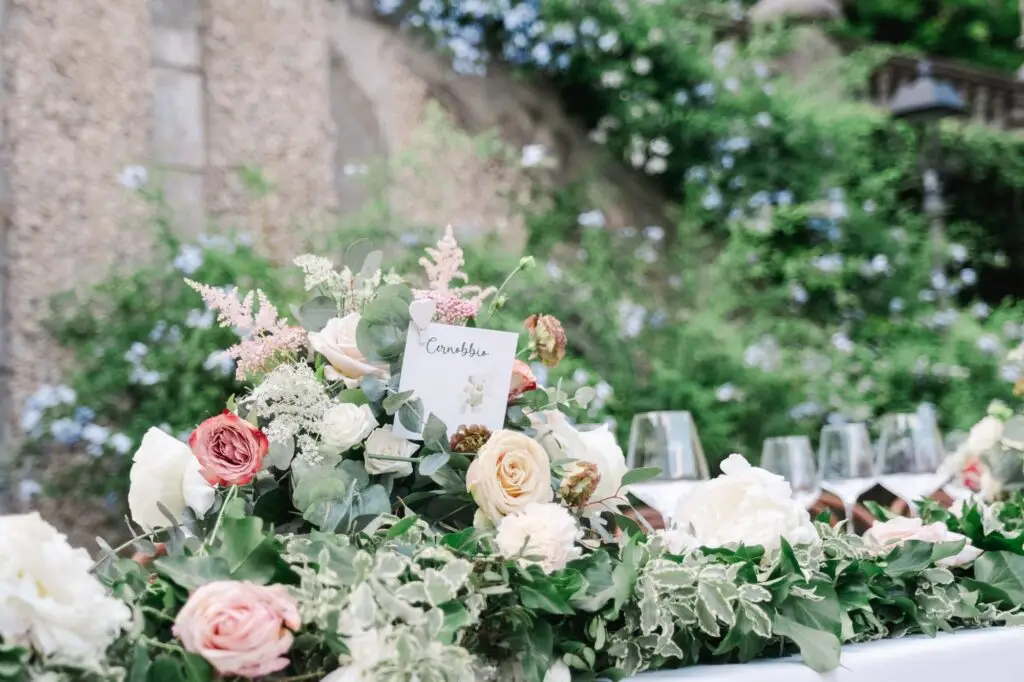 Close-up of floral centerpiece with roses and greenery, table card reading “Cernobbio” at Villa Pizzo wedding.