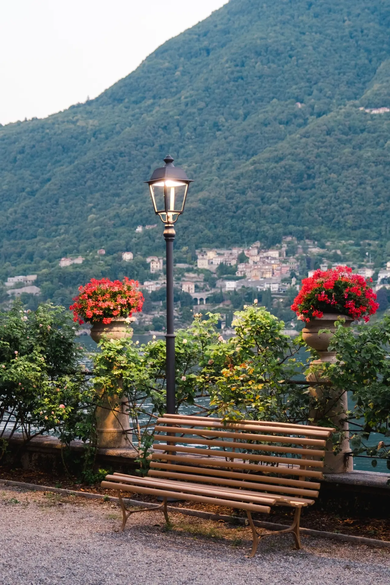 Evening garden detail with a wooden bench and lamppost overlooking the Italian lakeside, surrounded by flowers.