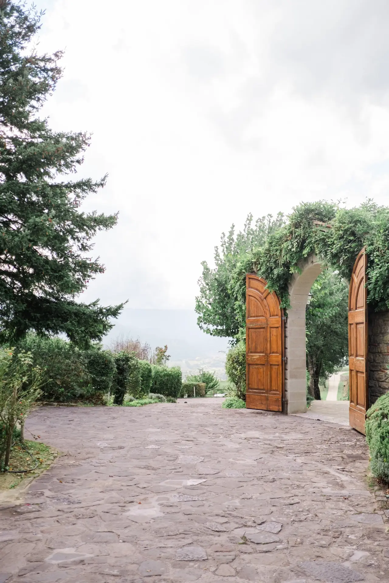 Rustic stone arch with wooden doors opening to panoramic countryside views at Borgo Corsignano wedding venue in Tuscany, Italy – a romantic setting for destination weddings