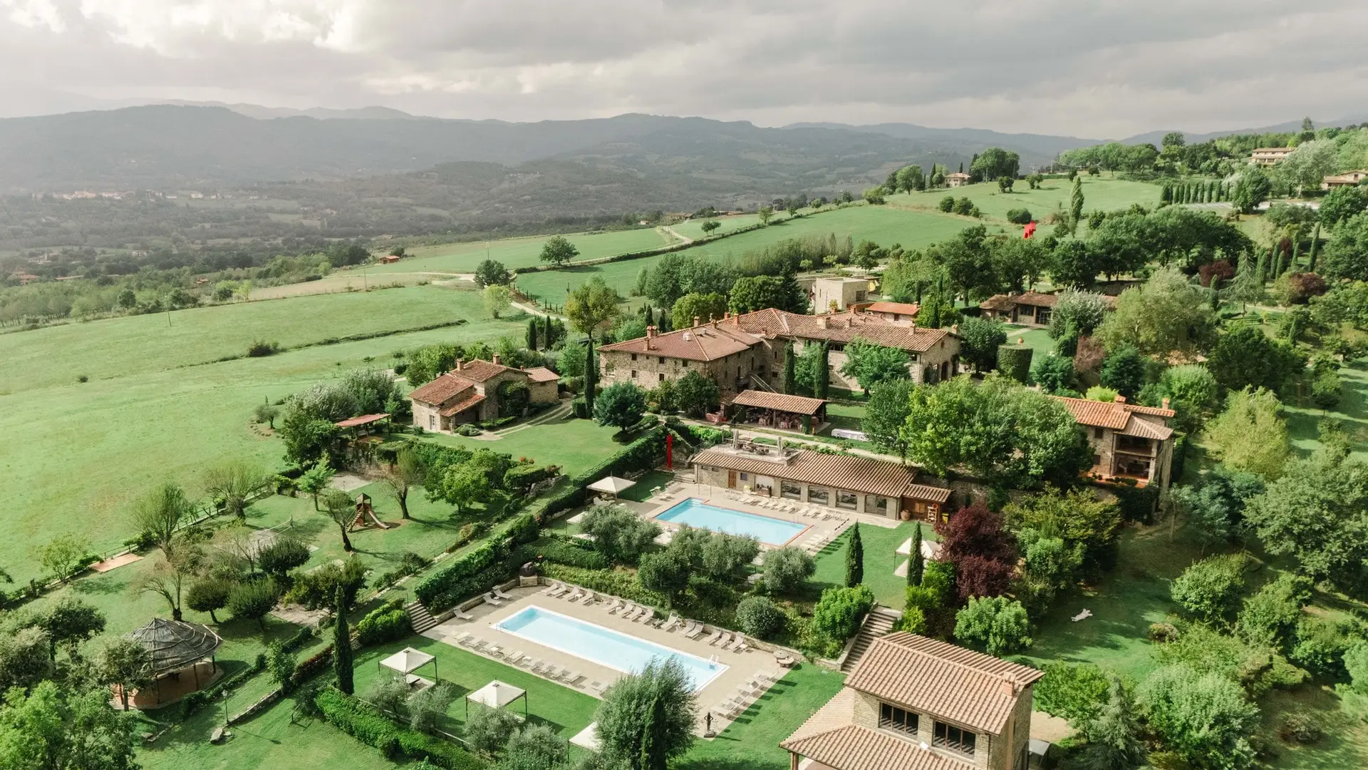 Aerial view of Borgo Corsignano luxury wedding venue in Tuscany, Italy – surrounded by rolling hills, olive trees, and swimming pools, perfect for destination weddings in the Italian countryside.