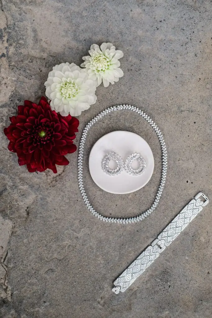 Flat lay of bridal jewelry set with diamond necklace, earrings, and bracelet styled with flowers for a luxury wedding in Tuscany, Italy.