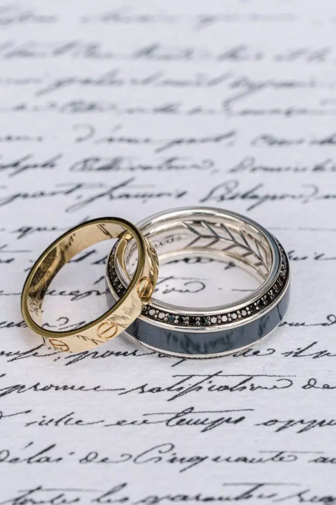 Artistic shot of two wedding bands, one gold Cartier ring and one silver ring with black details, placed on a handwritten love letter