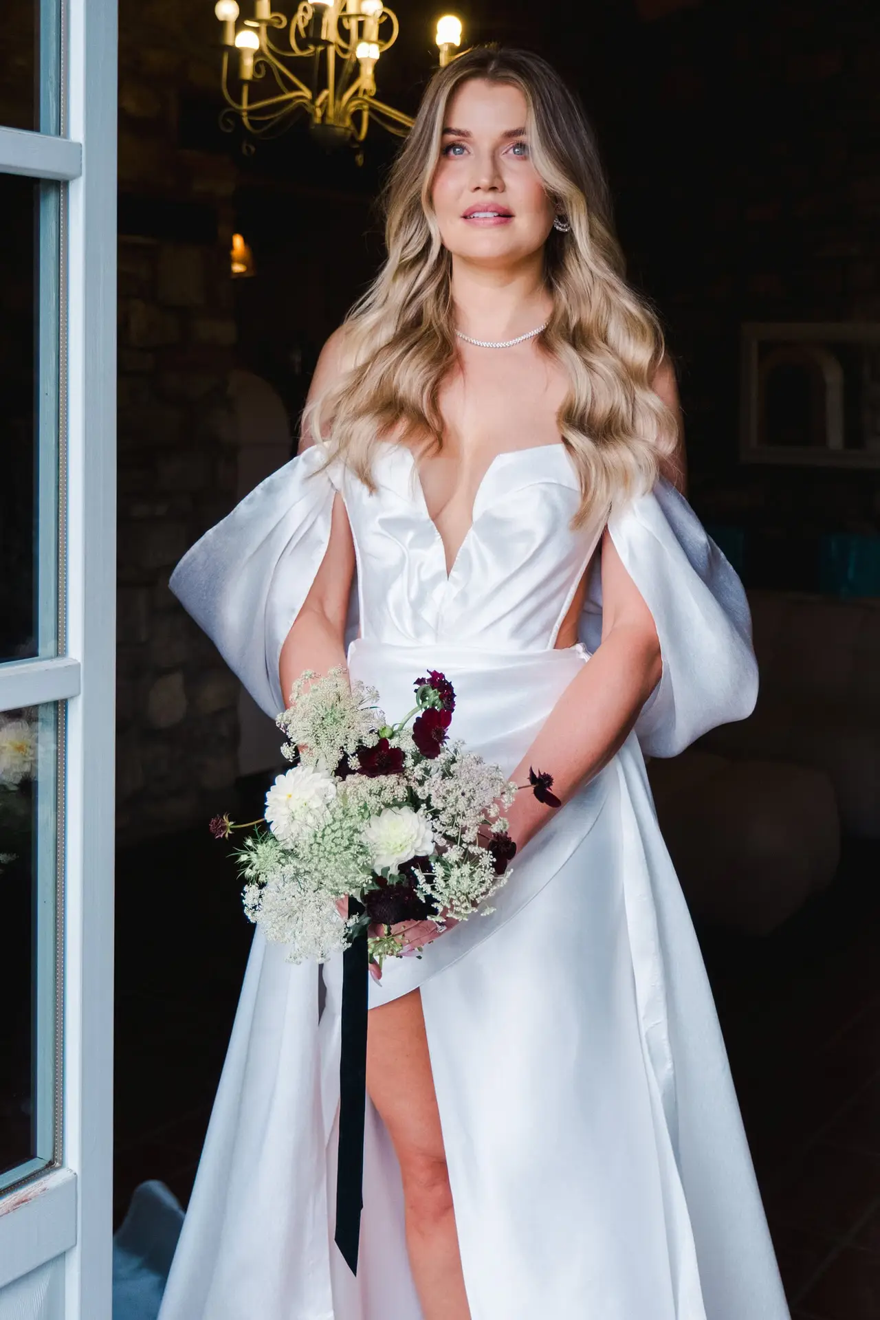Bride holding bouquet of white and burgundy flowers, standing gracefully in her wedding dress in Tuscany