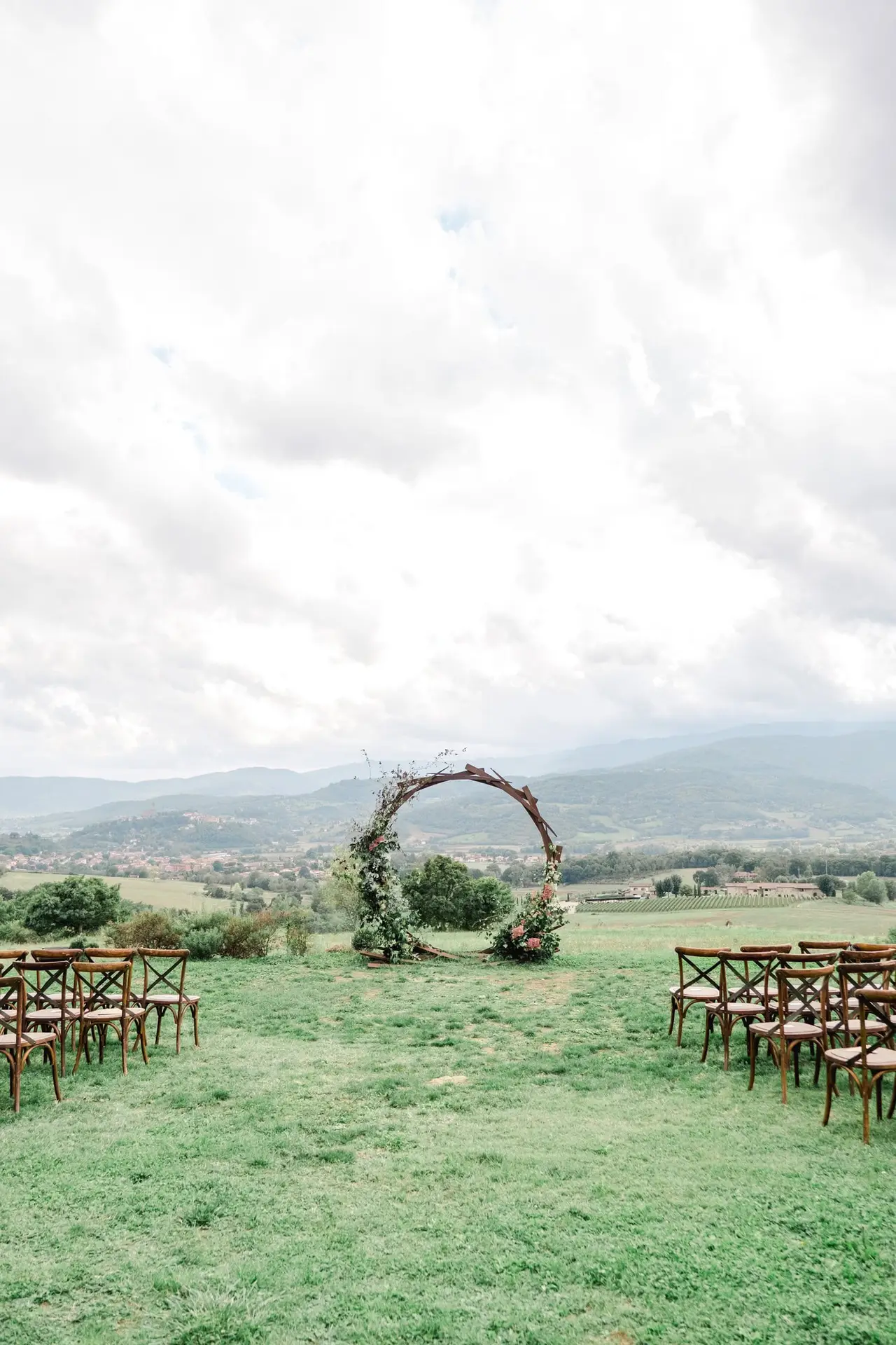 Rustic circular wedding arch adorned with greenery and flowers, set in the Tuscan countryside with panoramic vineyard views, ready for an outdoor ceremony