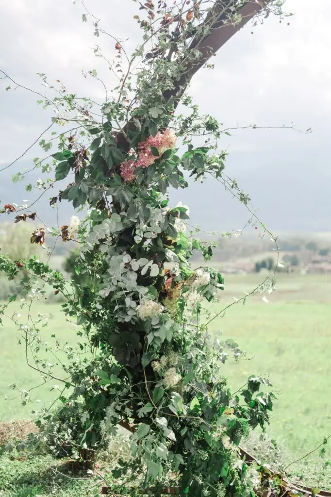Floral details of a Tuscan wedding arch with ivy, white blossoms, and lush greenery against a scenic countryside backdrop