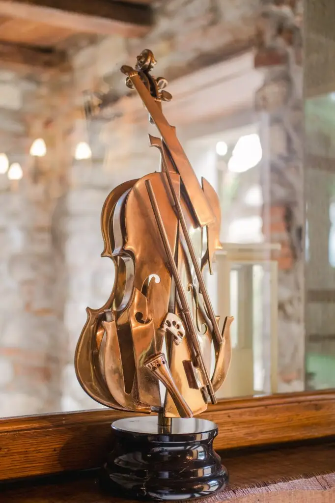 A close-up of a bronze decorative violin sculpture displayed on a wooden surface, reflecting soft indoor light.