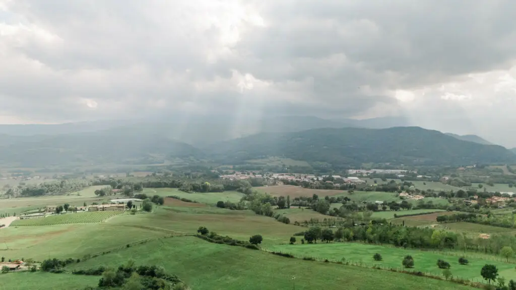 Panoramic aerial view of the green Tuscan countryside, bathed in dramatic sunlight breaking through the clouds.