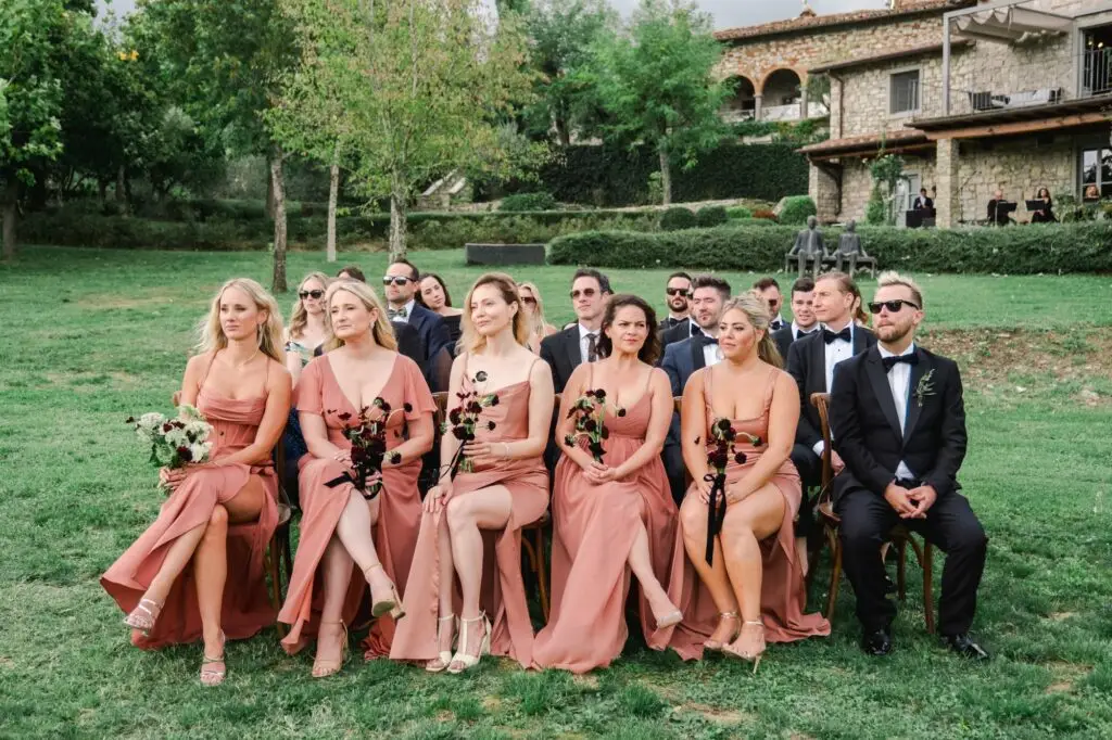 Bridesmaids in elegant terracotta gowns holding bouquets, seated front row at the sophisticated outdoor ceremony at Borgo di Corsignano.