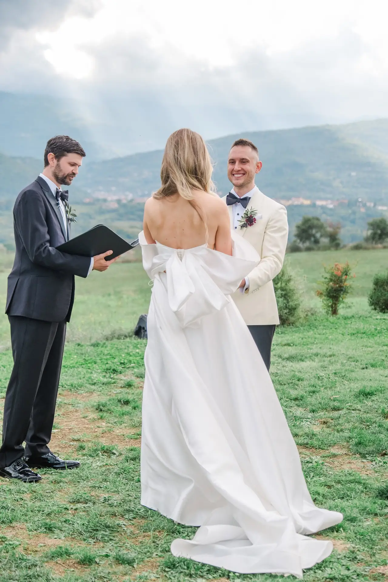 Back view of the bride facing the groom and officiant, framed by breathtaking Tuscan hills at Borgo di Corsignano.