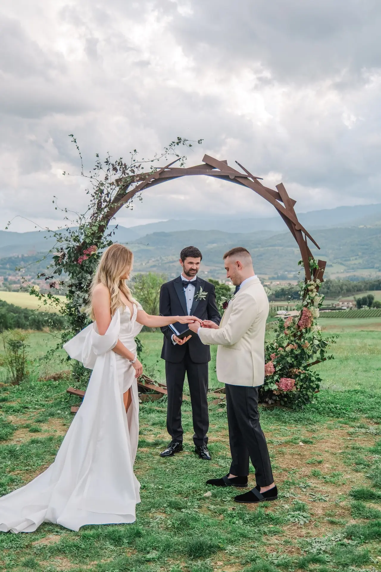 A magical ceremony in the Tuscan hills — vows exchanged beneath a bespoke floral arch, with the rolling countryside of Borgo di Corsignano as the backdrop.