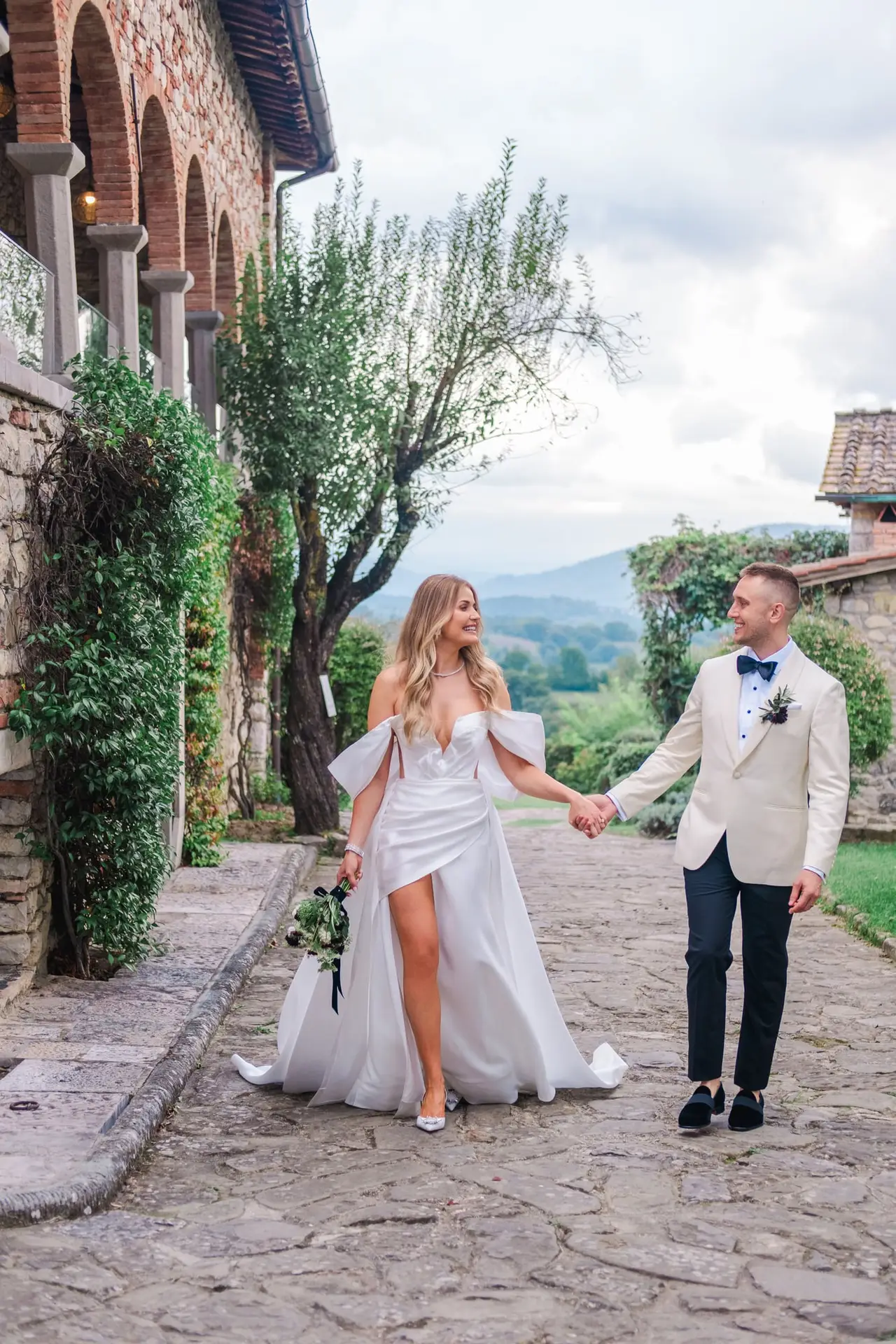 Hand in hand, walking through the rustic stone paths of Borgo di Corsignano — a true fairytale setting for a luxury Tuscan wedding, captured by Julien Boyer.