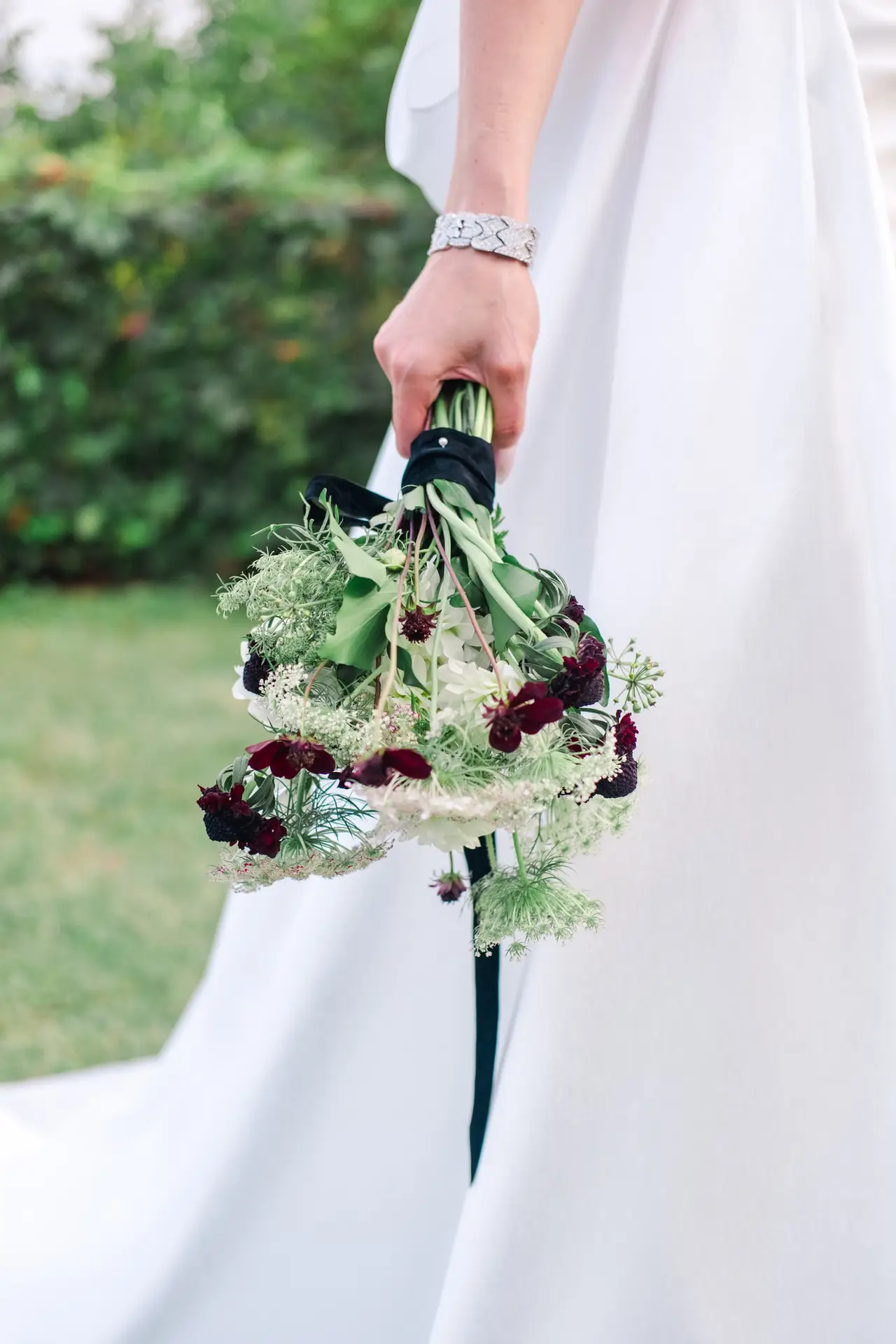 Bride holding a refined bouquet of greenery and deep purple accents, a detail captured at a luxury wedding in Tuscany.