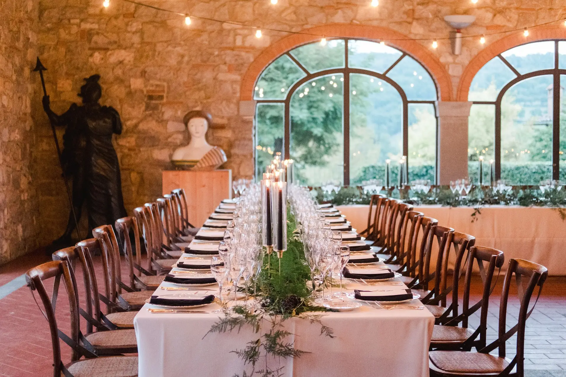 Long wedding reception table styled with greenery and candles inside a rustic stone hall at Borgo di Corsignano in Tuscany.