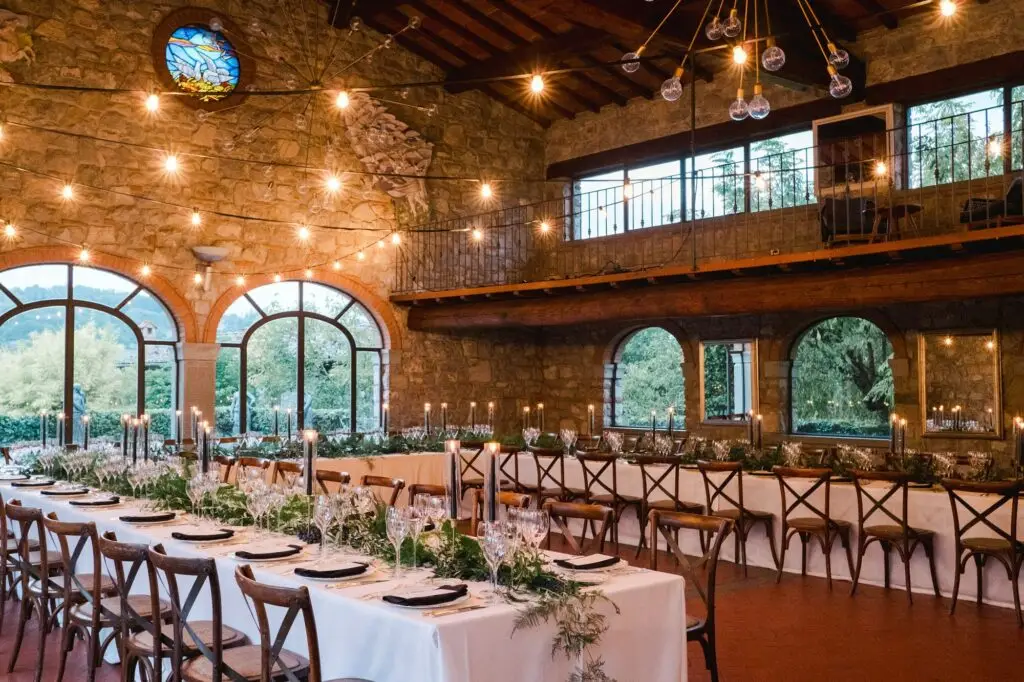 Elegant wedding reception at Borgo di Corsignano in Tuscany, with long white tables, chandeliers, and a warm glowing atmosphere, captured by Julien Boyer.