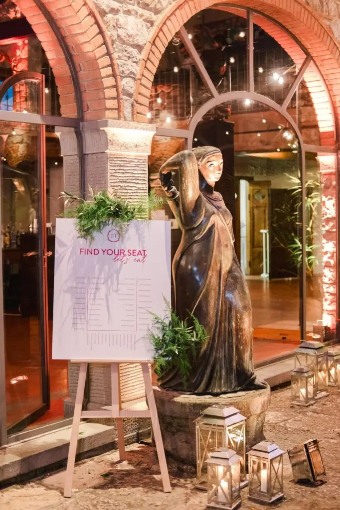 Wedding seating plan displayed at the entrance under stone arches with a classic statue and glowing lanterns, setting a chic and elegant tone, captured by Julien Boyer.