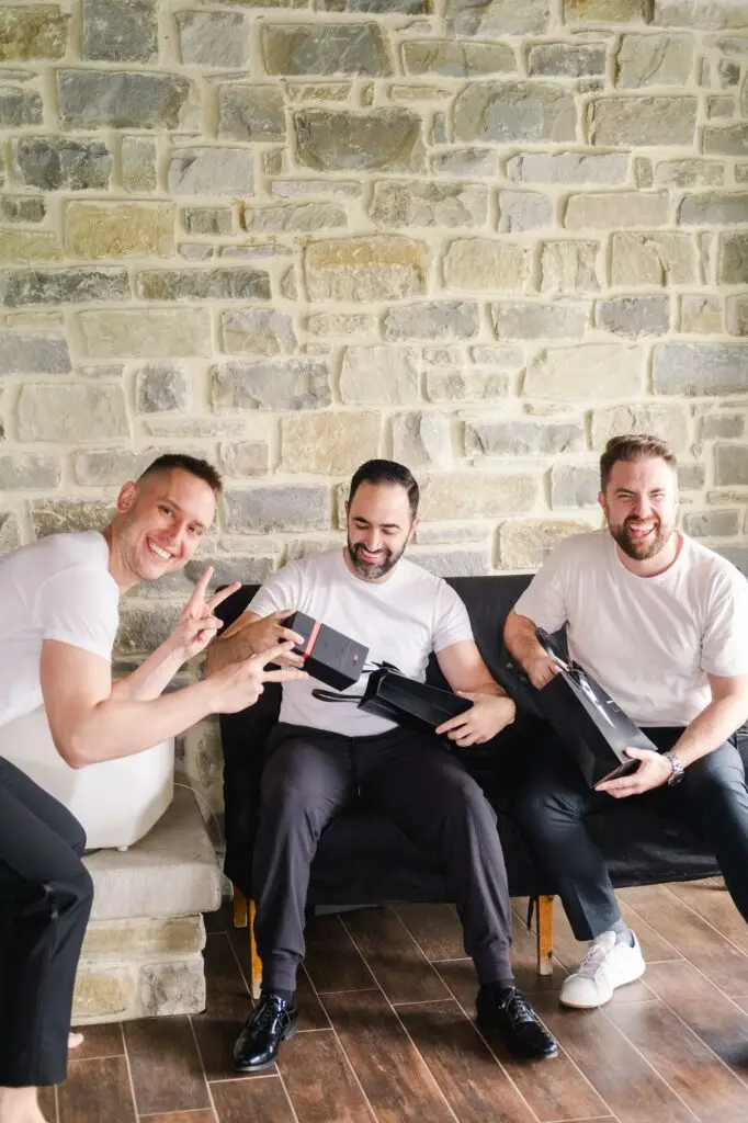 Groom and groomsmen sharing gifts and laughing during destination wedding preparations in Tuscany, Italy.