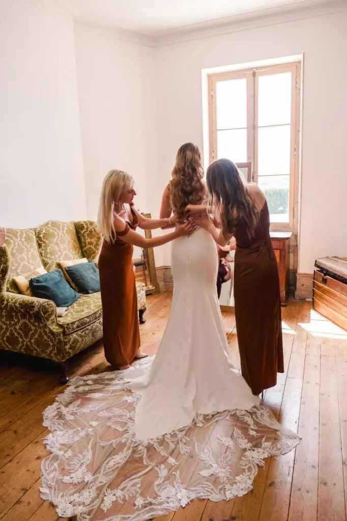 Un instant suspendu lors des préparatifs : la mariée se fait aider à fermer sa robe, baignée par la lumière naturelle du château.