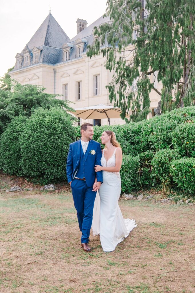 Couple de mariés marchant main dans la main dans le parc du Château Fengari, séance photo de mariage réalisée par un photographe de mariage près de Bordeaux.