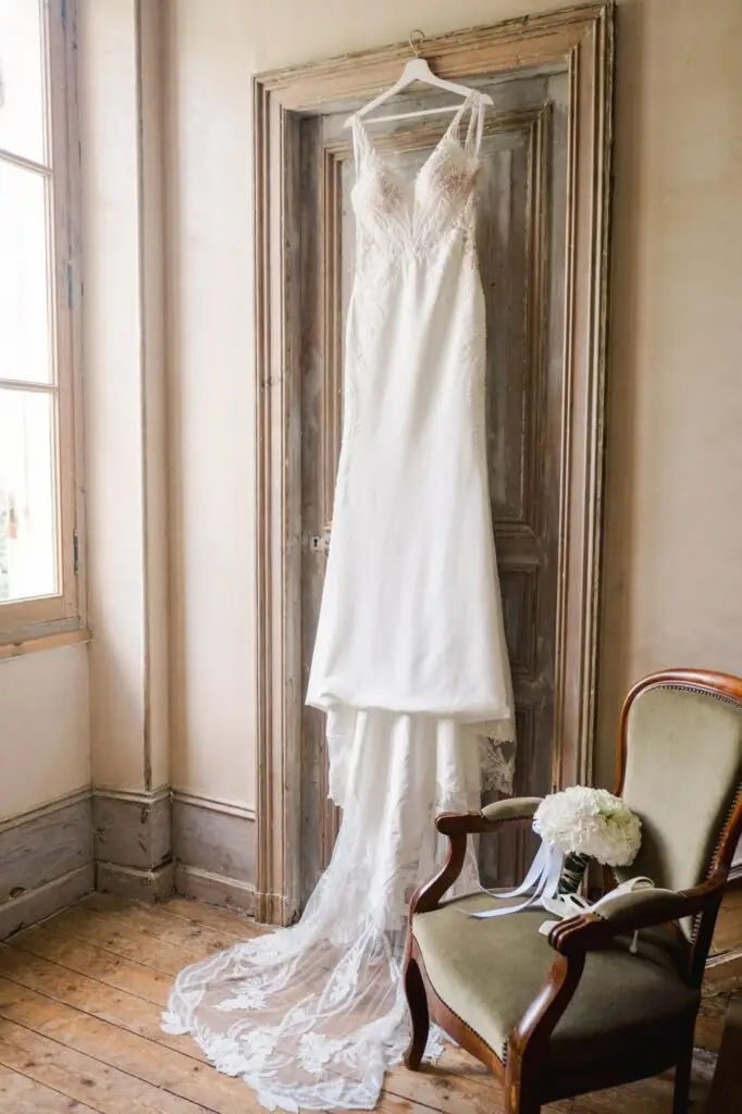 Robe de mariée suspendue lors des préparatifs au Château Fengari à Bordeaux, dans une pièce lumineuse au décor ancien.