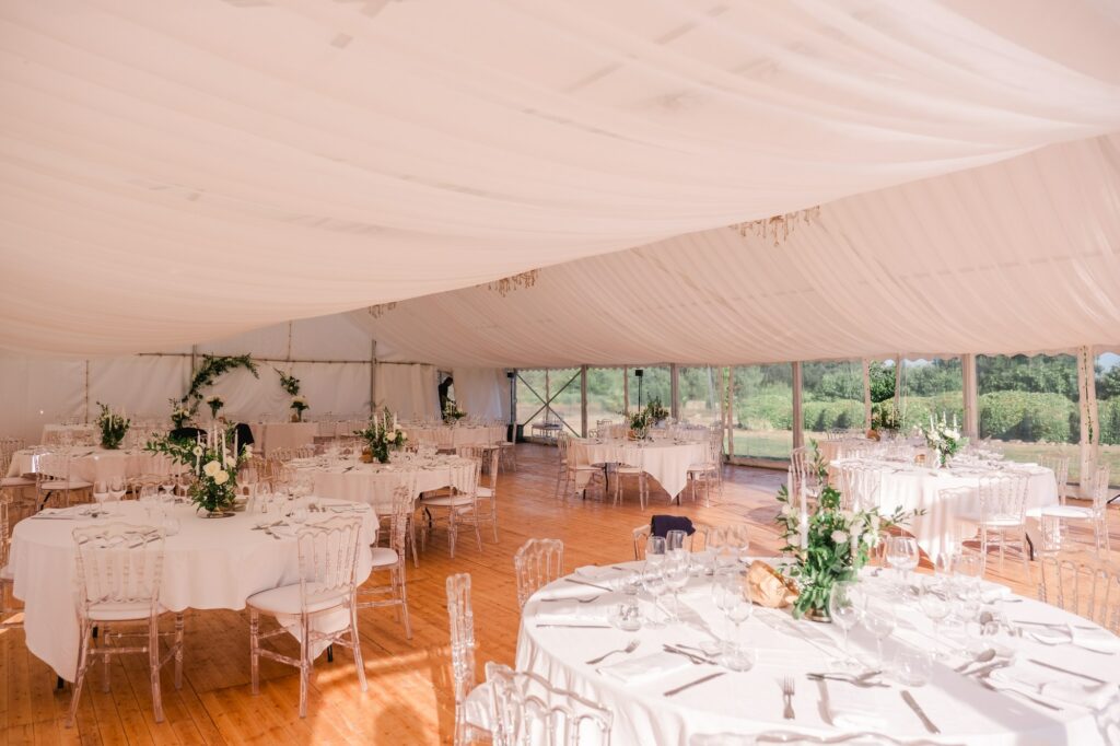 Salle de réception du mariage installée sous une grande tente blanche au Château Fengari, près de Bordeaux, tables rondes dressées avec décoration florale et lumière naturelle, photographie réalisée par un photographe de mariage.