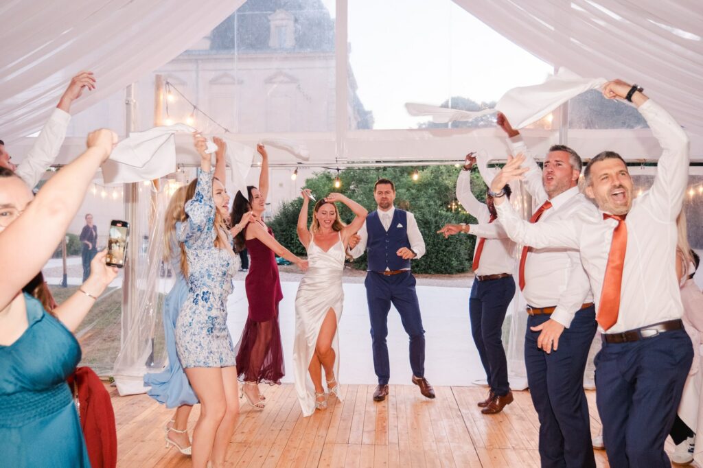 Alt : Groupe d'invités dansant lors d'un mariage sous tente, capturé par un photographe professionnel à Bordeaux, avec ambiance conviviale et festive.