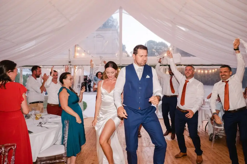 Les mariés dansent entourés de leurs invités pendant la soirée de mariage sous la tente de réception du Château Fengari, près de Bordeaux, ambiance festive et conviviale immortalisée par un photographe de mariage.