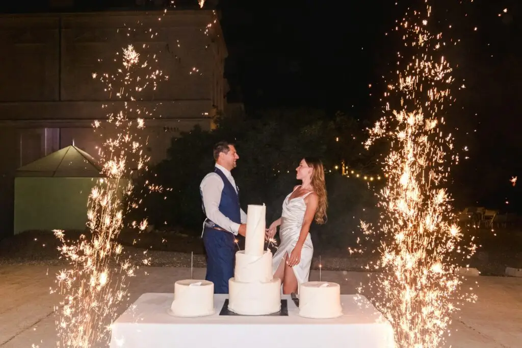 Photographe de mariage à Bordeaux capturant un instant magique entre un couple devant un gâteau et des feux d'artifice en soirée.